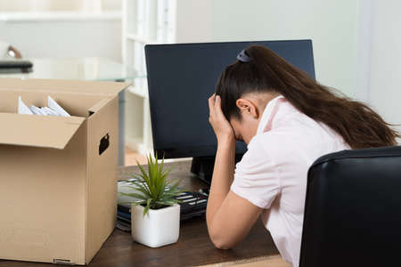 Dismiss Young Businesswoman With Belongings Sitting At Desk In Officeの写真素材