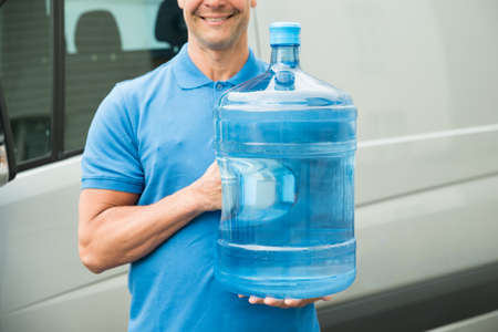 Close-up Of Delivery Man In Blue Uniform Carrying Large Water Bottleの写真素材