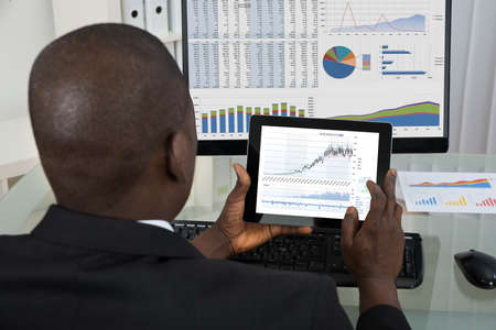 Rear View Of Young African Businessman Analyzing Graph On Digital Tablet In Officeの写真素材
