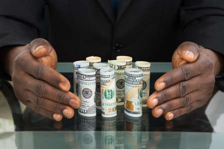 Close-up Of Businessman Hands Protecting Banknotes At Glass Deskの写真素材
