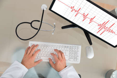 Doctor With Computer At Desk Showing Cardiogram On Screen