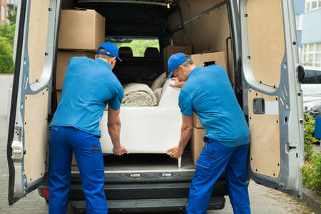 Two Male Workers In Blue Uniform Adjusting Sofa In Truckの写真素材