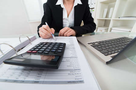 Close-up Of Businesswoman Calculating Invoice With Calculator