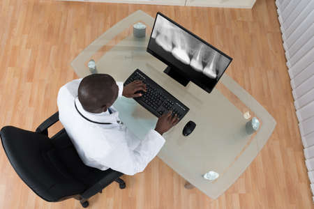 Young African Dentist Analyzing X-ray Teeth On Screen Of Computer At Deskの写真素材