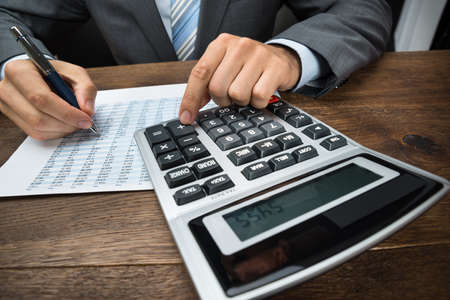 Close-up Of Businessperson Doing Calculation With Calculator In Officeの写真素材