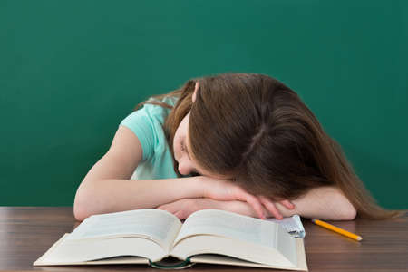 Tired Student With Books And Pencil Sleeping At Desk In Classroom