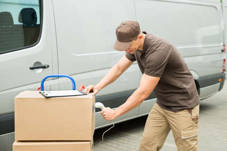 Young Delivery Man Scanning Cardboard Boxes With Barcode Scanner