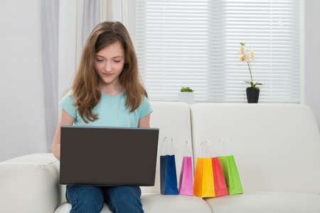 Happy Girl Using Laptop With Small Shopping Bags On White Sofaの写真素材