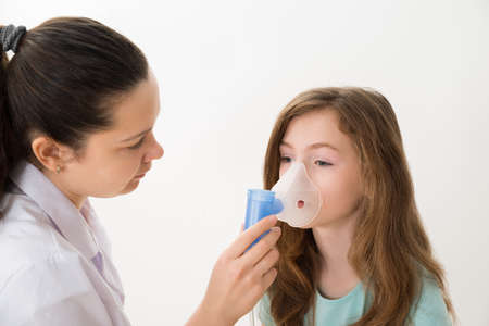 Young Female Doctor Using Inhaler Mask On Girlの写真素材