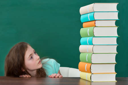 Afraid Girl Looking At Pile Of Colorful Books At The Wooden Tableの写真素材