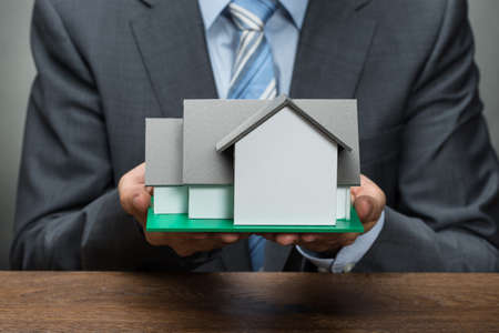 Close-up Of Businessman Holding House Model At Wooden Deskの写真素材