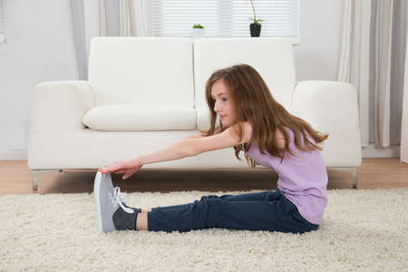 Cute Girl Exercising In Front Of Sofa On Carpet In Living Room