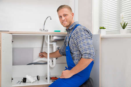 Happy Male Plumber Repairing Faucet In Kitchen Sinkの写真素材