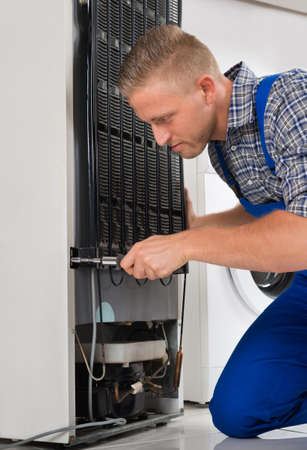 Male Worker Repairing Refrigerator With Screwdriver In Houseの写真素材