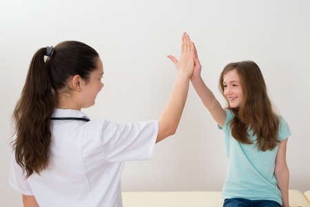 Young Female Doctor Giving High Five To Girl In Clinicの写真素材