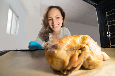 Happy Woman Putting Chicken Tray View From Inside The Kitchen Ovenの写真素材