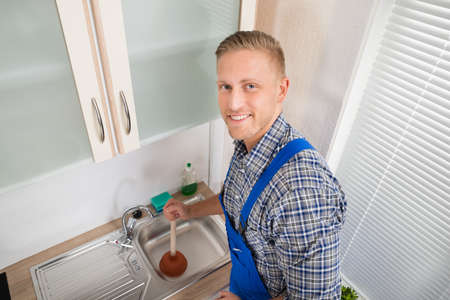 Young Happy Plumber Using Plunger In Kitchen Sinkの写真素材