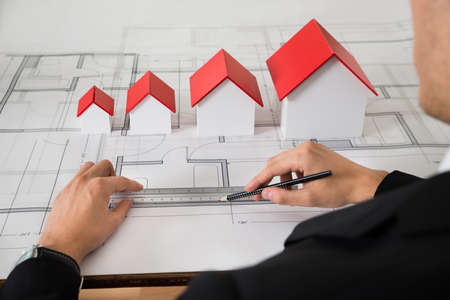 Close-up Of Architect With Different Size House Models On Blueprint In Officeの写真素材