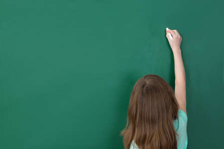 Girl Writing With Chalk On Green Chalkboard In Classroomの写真素材