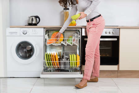 Woman Standing In Kitchen Removing Bowls From Dishwasherの写真素材