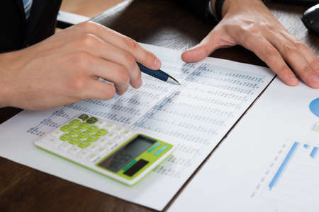 Close-up Of Businessperson Working With Accounting Document At Desk