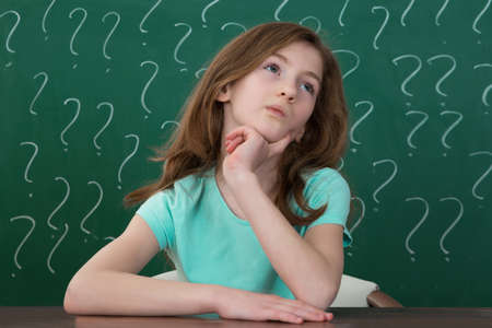 Contemplating Girl Sitting At Desk With Question Mark Drawn In Chalk On The Chalkboardの写真素材