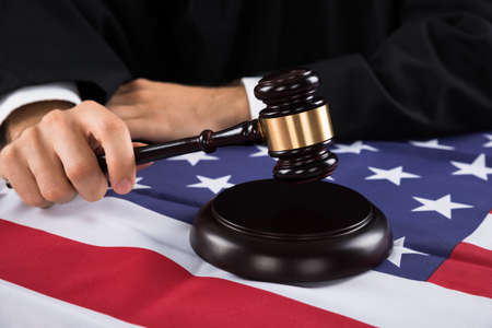 Close-up Of Judge Hands With Gavel And American Flag At Desk