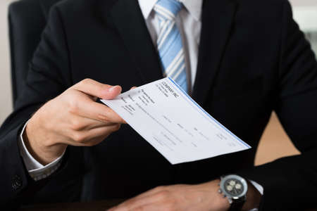 Close-up Of Businessman Hands Giving Cheque In Office