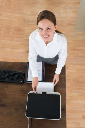 High Angle View Of Young Businesswoman Using Printer At Desk In Officeの写真素材