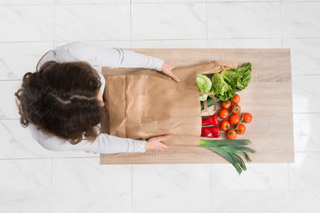 High Angle View Of Young Woman Removing Vegetables From Shopping Bagの写真素材