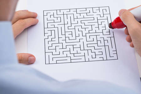 Close-up Of Person Hand With Maze On Paper And Red Marker