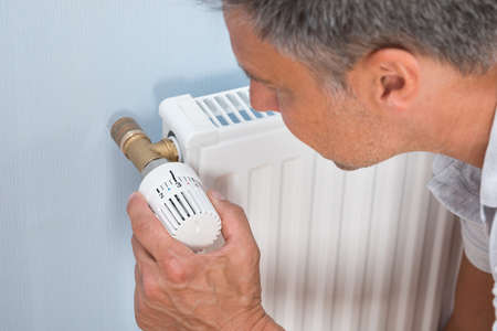 Man Adjusting Temperature Of Radiator Using Thermostat