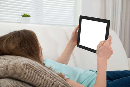 Girl Lying On Sofa Holding Digital Tablet With Blank Display