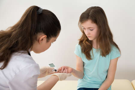 Doctor In Labcoat Measuring Blood Sugar Level Of Girl With Glucometerの写真素材