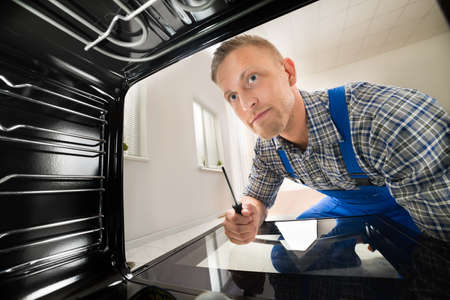 Young Repairman With Screwdriver Fixing Kitchen Ovenの写真素材