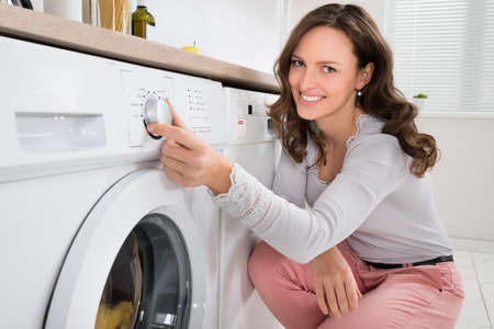 Close-up Of Young Woman Pressing Button Of Washing Machine In Kitchenの写真素材