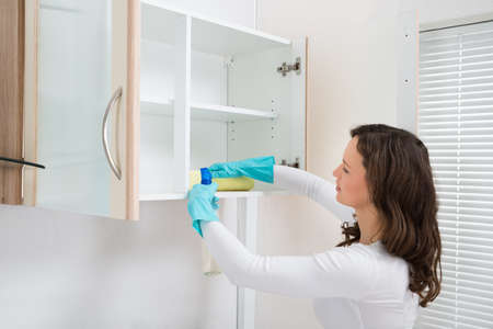 Young Woman Cleaning Shelf With Rag And Detergent Spray Bottle