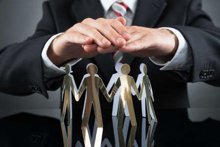 Close-up Of Businessperson Protecting Cutout Figures At Deskの写真素材