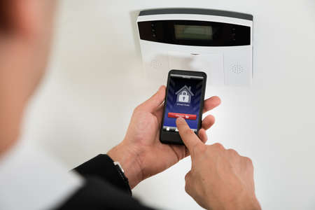 Close-up Of Businessperson Hands Disarming Security System Of Door With Mobile Phone