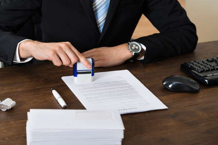 Close-up Of Businessman Stamping Contract Document Paper At Deskの写真素材