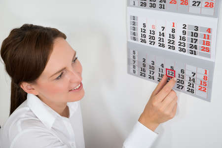Close-up Of Young Businesswoman Placing Red Mark On Calendar Dateの写真素材