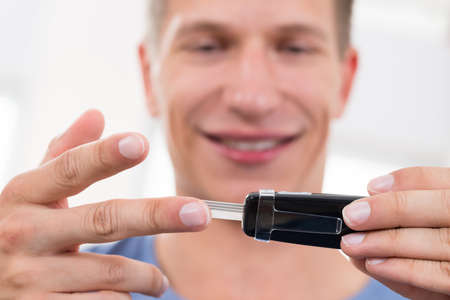 Close-up Of Young Happy Man Checking Blood Sugar Level With Glucometerの写真素材
