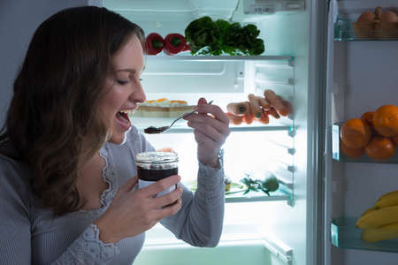 Young Woman Eating In Front Of Fridge In Kitchen