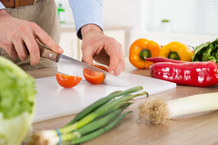 Close-up Of Male Hands Cutting Tomato At Countertop In Kitchenの写真素材