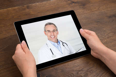 Close-up Of Person Videochatting With Doctor On Digital Tablet At Desk