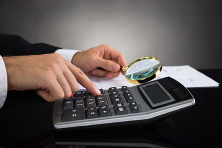 Close-up Of Businessperson Inspecting Invoice With Magnifying Glass And Calculatorの写真素材