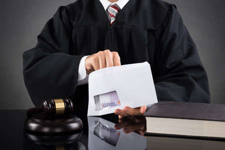 Close-up Of Judge Putting Money In Envelope At Desk In Courtroom
