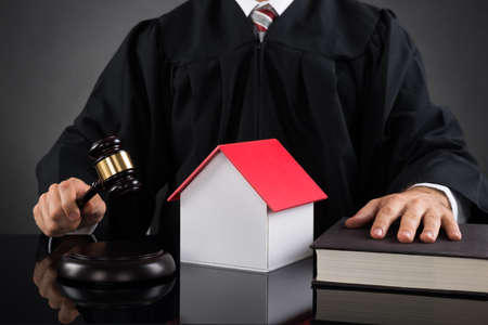 Close-up Of Judge Holding Gavel With House Model At Deskの写真素材