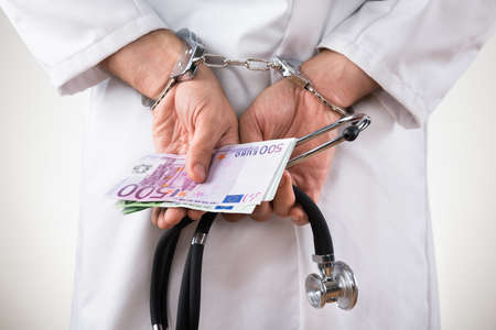 Close-up Of A Doctor Hands With Euro Bank Notes And Handcuffsの写真素材