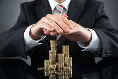 Close-up Of Businessman Saving Pile Of Coins At Deskの写真素材